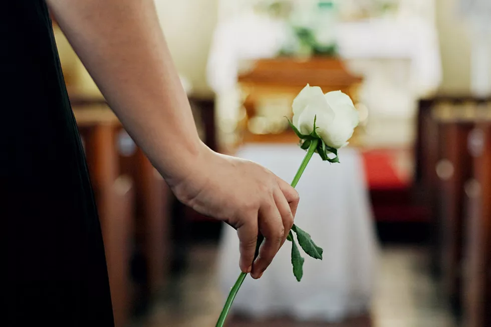 Weibliche Hand hält weiße Rose bei einer Trauerfeier